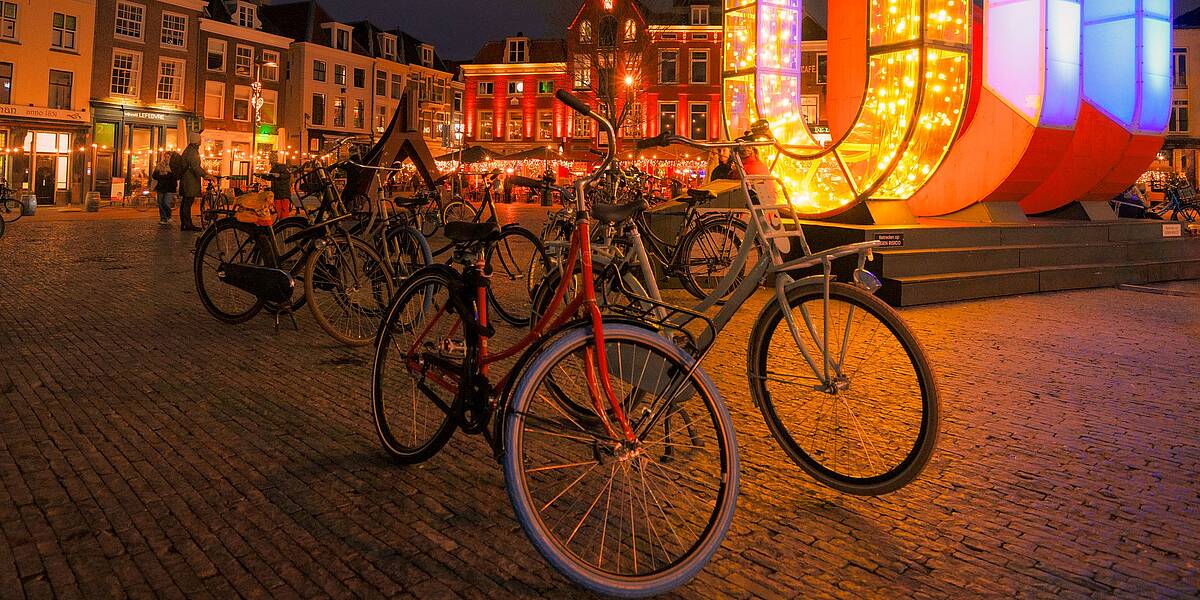 Link naar foto in Flickr: fietsen geparkeerd op De Neude in de avond. Met op de achtergrond 3 lichtgevende letters U.
