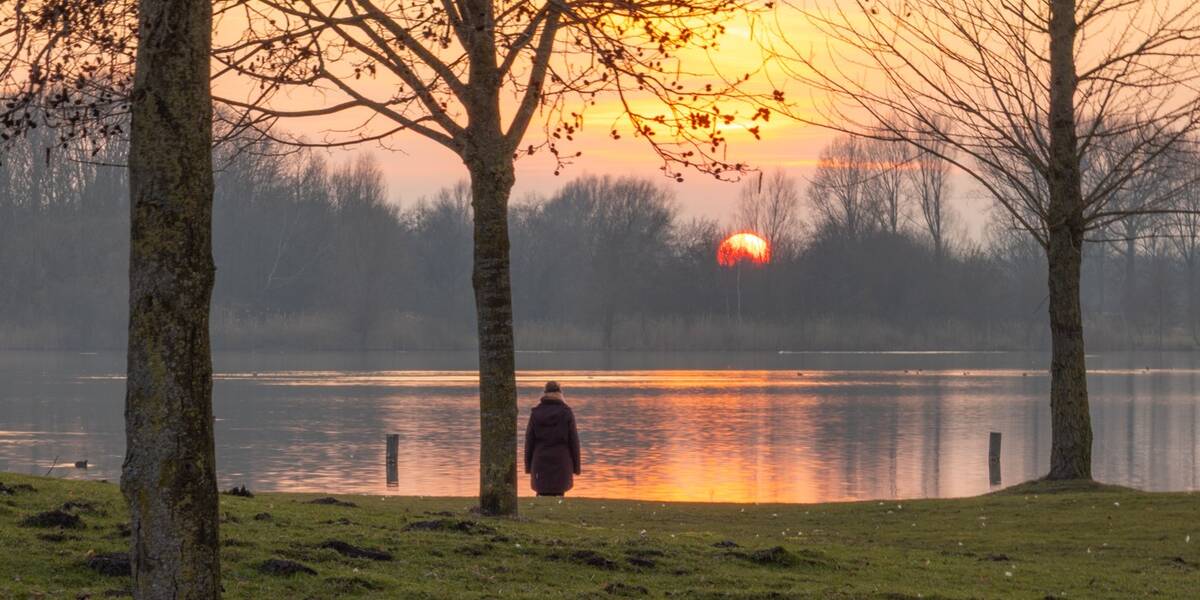 Een vrouw staat in de avondzon voor de Haarrijnseplas.