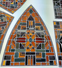 panelen met glas-in-lood, vooral roodbruine en groengrijze tinten, abstracte vormen met rechte lijnen, soms diagonaal. De panelen zijn symmetrisch en passen in een gotisch raam