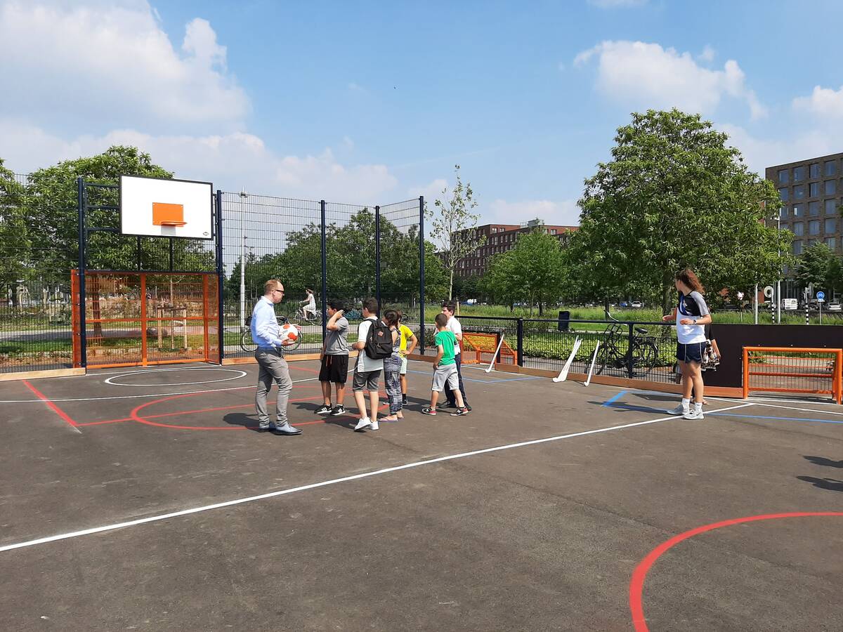 Wethouder Eelco Eerenberg trapt balletje met kinderen bij de officiële opening van de nieuwe sportkooi. 