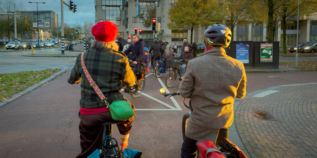 Link naar foto in Flickr: Daalsesingel in Utrecht. Wachten voor het stoplicht met een bundel zonlicht die valt op twee stijlvol geklede fietsers.