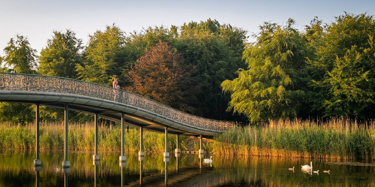 Link naar foto in Flickr: twee mensen lopen in de avondzon over de Lelievijverbrug in het Maximapark.