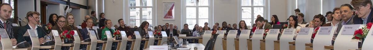 Foto van een gevulde raadszaal in het stadhuis. Op de stoelen links en rechts zitten de raadsleden uit de periode 2026-2030. In het midden is de publieke tribune zichtbaar.