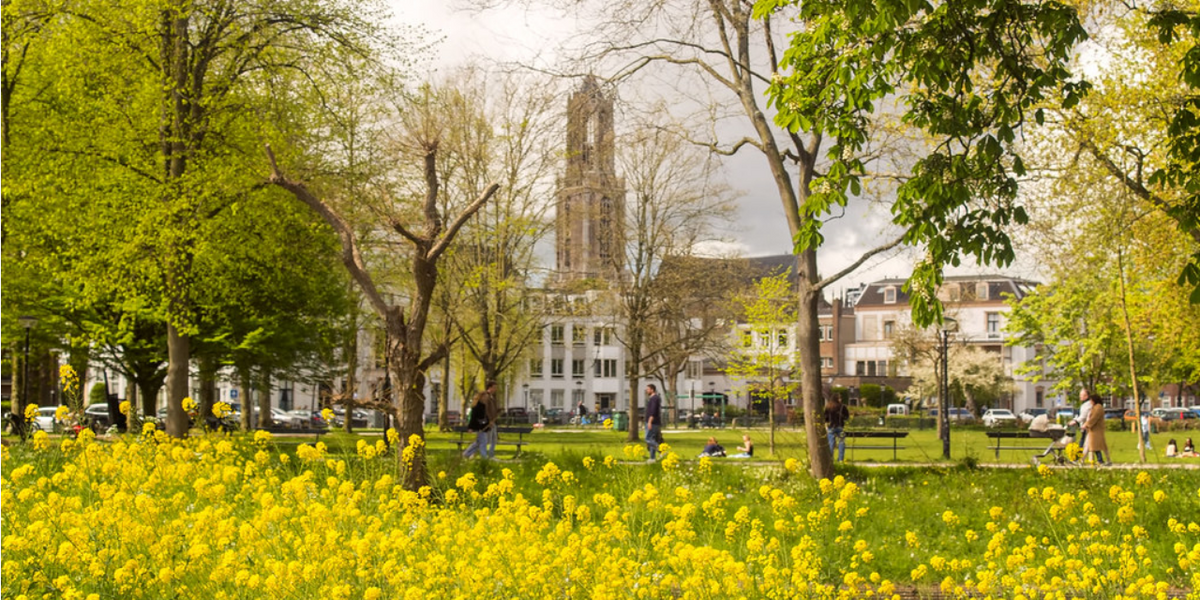 Link naar foto in Flickr: mensen wandelen in park Lepelenburg. Met bloeiende bloemen op de voorgrond. Op de achtergrond de Dom.
