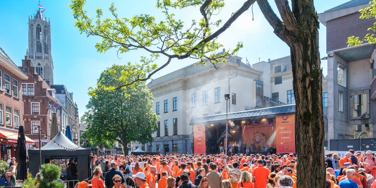 Mensen voor het stadhuis bij een muziekpodium op Koningsdag 2025.