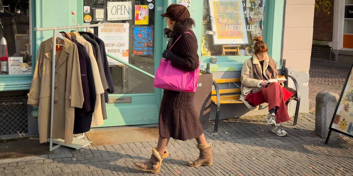Link naar foto in Flickr. Een vrouw loopt langs de vintagewinkel CAFCA aan de Oudegracht. Op een bankje voor de winkel zit een vrouw een kopje koffie te drinken. 