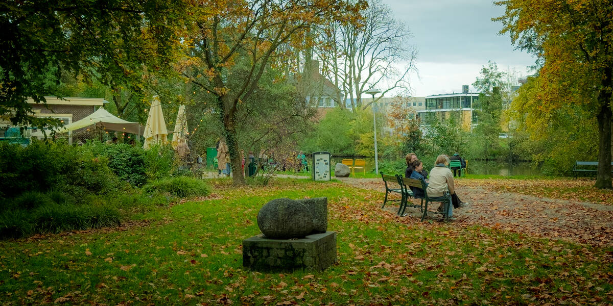Link naar foto in Flickr: mensen zitten op een bankje in Park Oog in Al. De eerste herfsbladeren liggen op de grond.