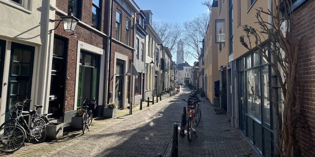 Zonnestralen gaan door de Korte Lauwerstraat, op de achtergrond De Dom en een strak blauwe lucht. 