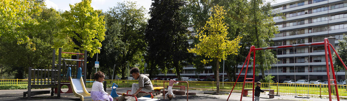 speeltuin met spelende kinderen, met daarachter bomen en een flatgebouw.