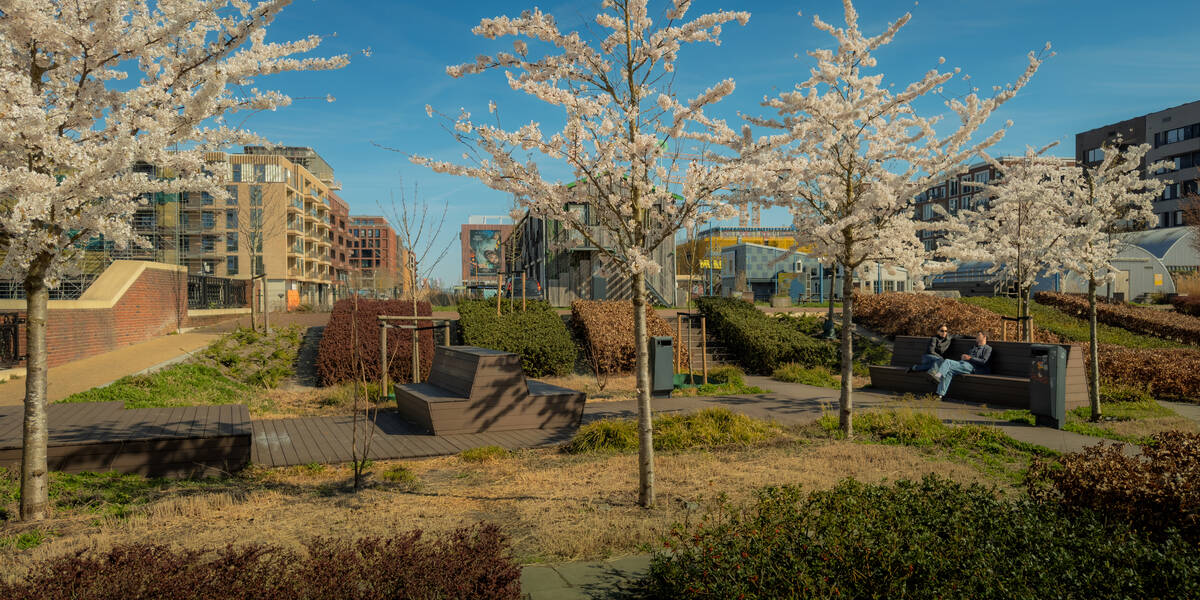 Link naar foto in Flickr: mensen zitten op een bank tussen bomen met bloesem in het Plantsoen van Boedapest. Op de achtergrond huizen. 