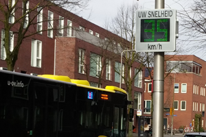 Een bus rijdt onder een snelheidsbord door.