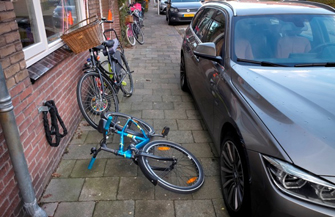 Auto half op stoep geparkeerd, fiets ligt op de stoep